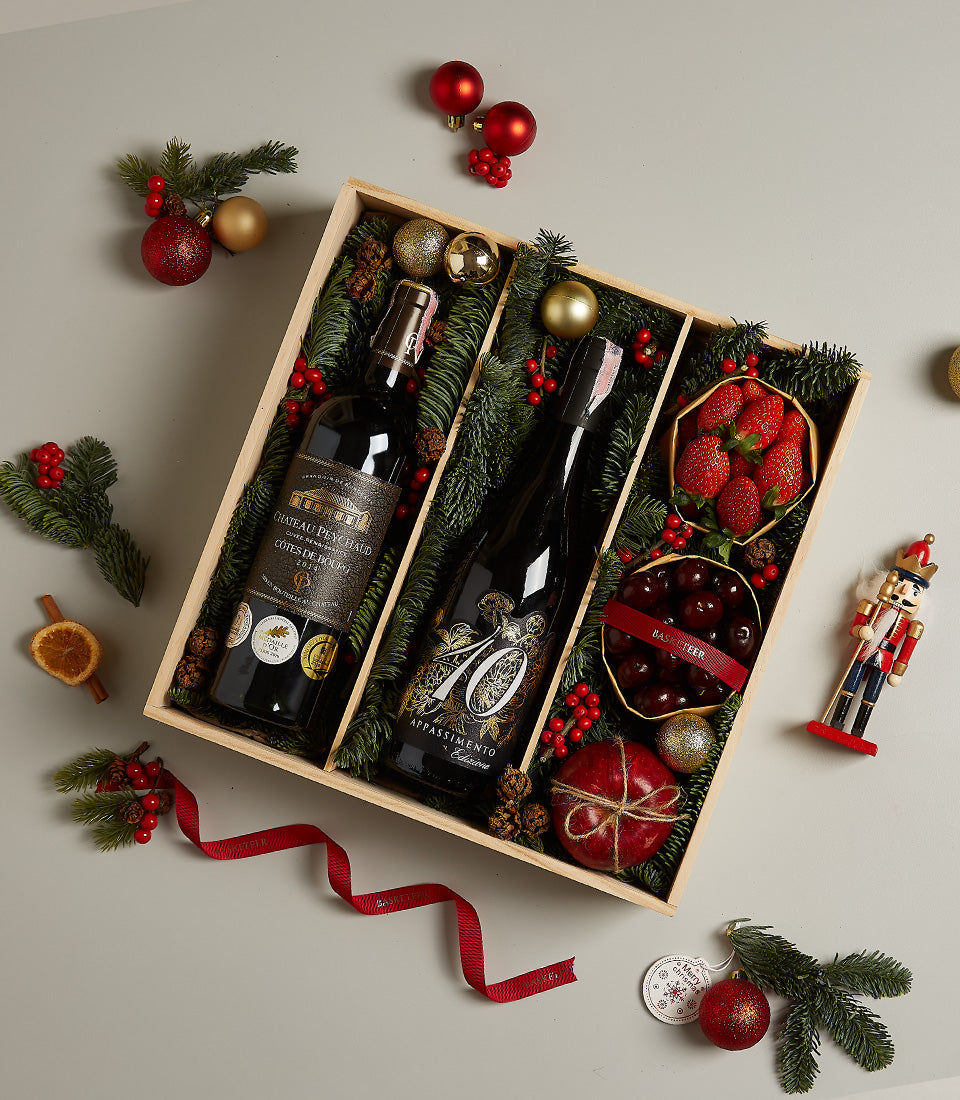 Elegant wine and fresh fruit holiday hamper with red wines, strawberries, cherries, and festive Christmas decorations