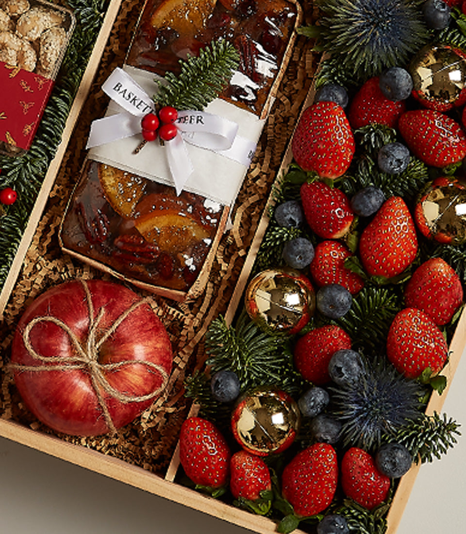 Festive wooden hamper with fruitcake, fresh berries, apple and Christmas greenery