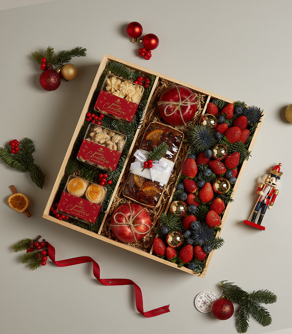 Festive wooden hamper with baked goods, fresh fruit, strawberries, blueberries, and Christmas decorations