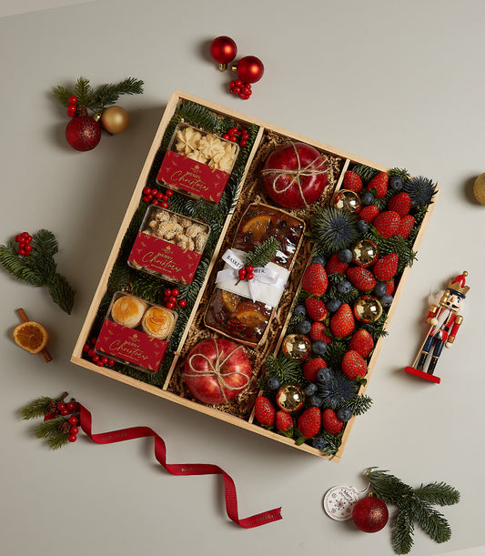 Festive wooden hamper with baked goods, fresh fruit, strawberries, blueberries, and Christmas decorations