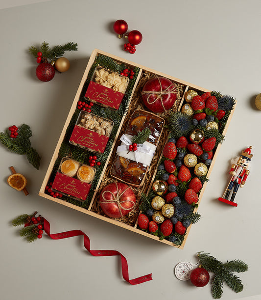 Luxury Christmas hamper with star cookies, fruitcake, fresh berries, chocolates, and festive ornaments in wooden gift box