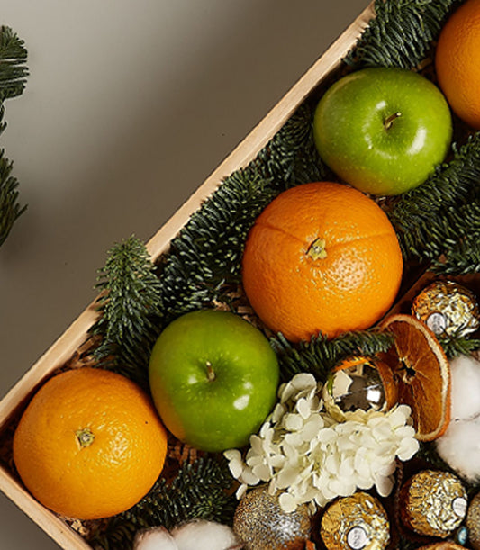 Festive wooden gift box with fresh apples, oranges, Ferrero Rocher chocolates, and gold Christmas ornaments