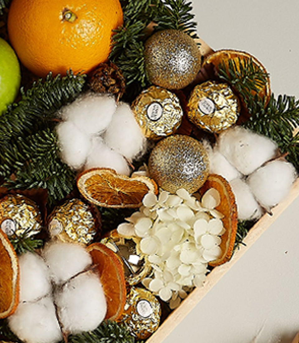 Festive wooden tray with fresh fruit, Ferrero Rocher chocolates, pine branches, and gold ornaments