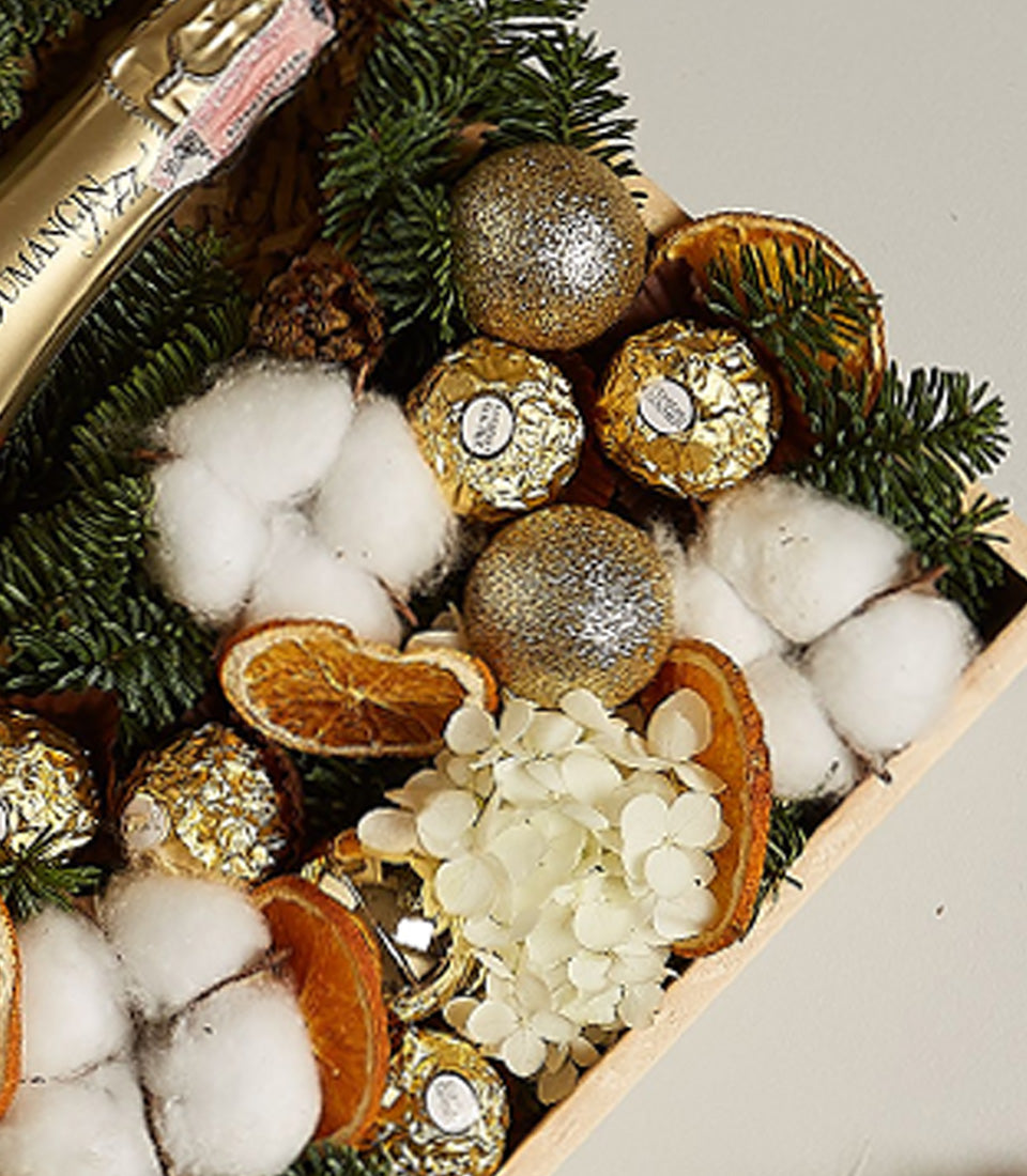 Luxury champagne and Ferrero Rocher gift box with gold ornaments, pine, and dried florals in wooden tray