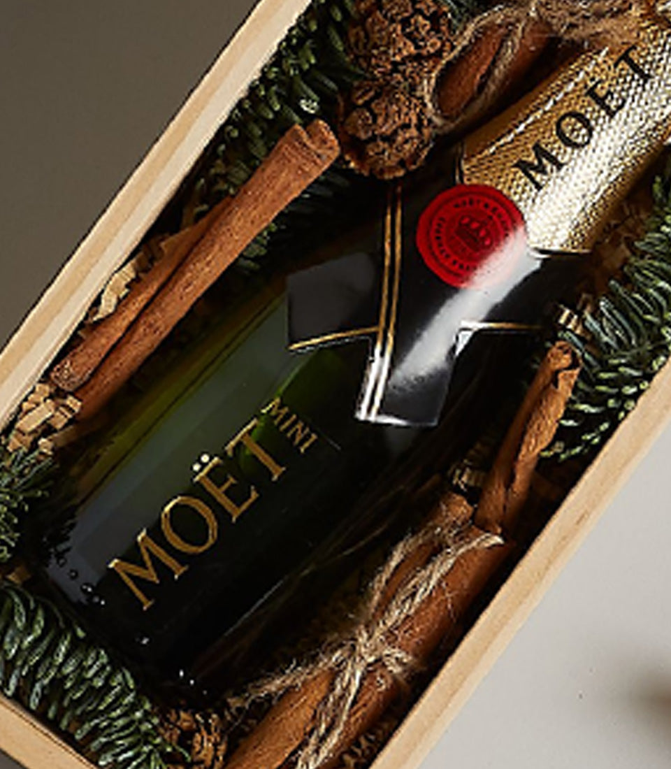 Golden Moët mini champagne gift box with cinnamon, pinecones, and festive ribbon for Christmas celebrations