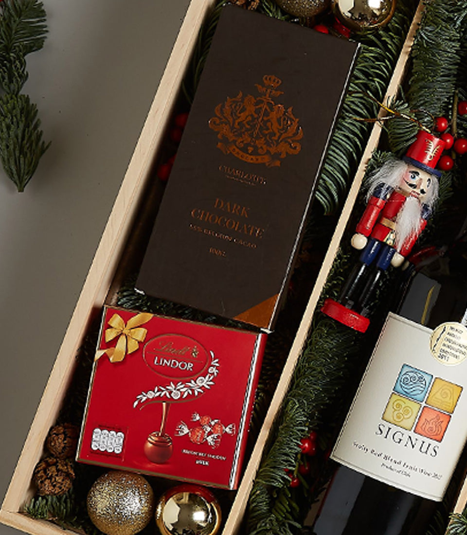 Premium red wine and gourmet chocolate holiday gift box with festive pine and gold accents