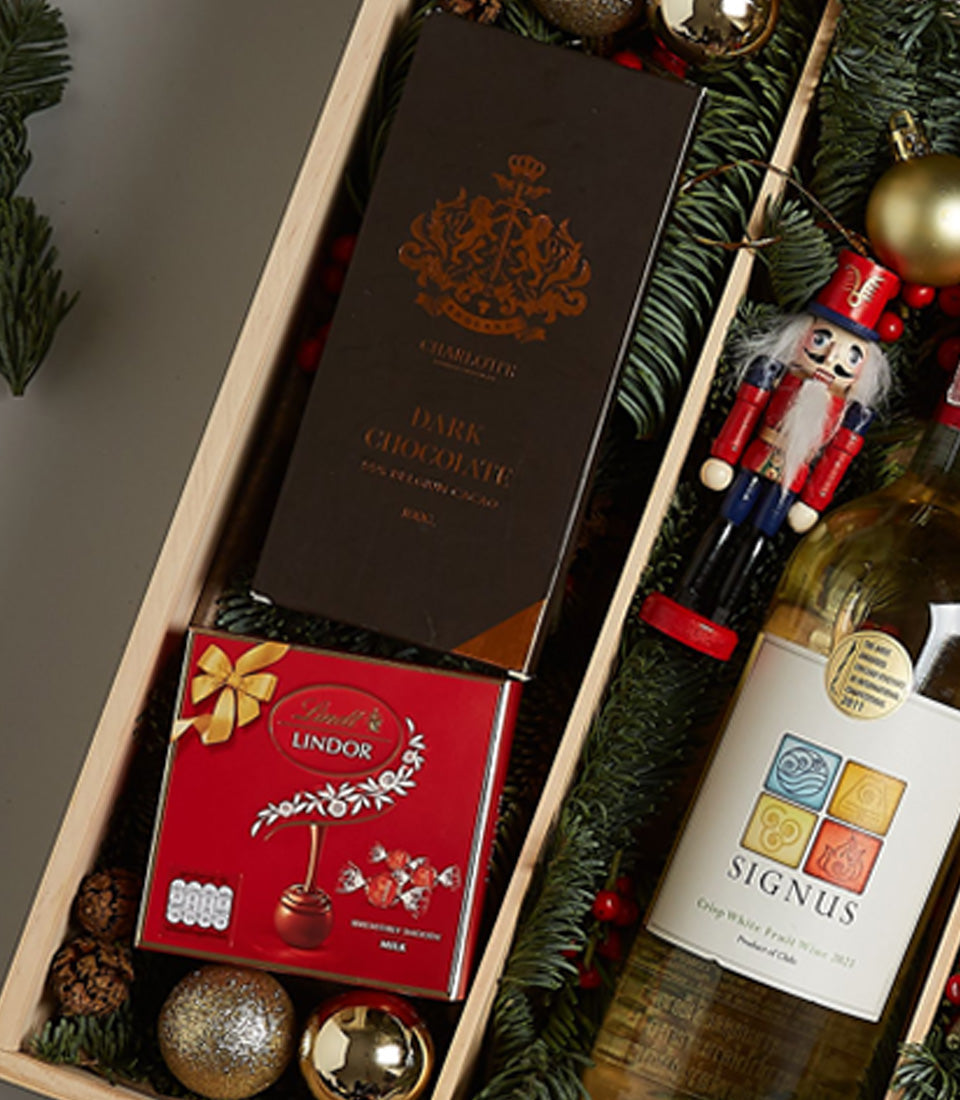 Elegant white wine gift hamper with dark chocolate, Lindor truffles, nutcracker ornament, and festive greenery in wooden box