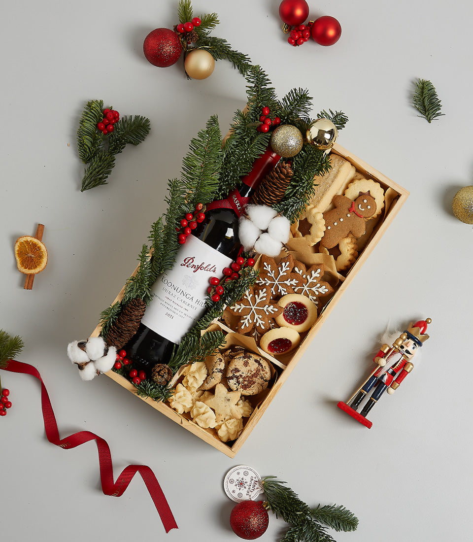 Festive red wine gift box with gingerbread cookies, shortbread, and Christmas decorations