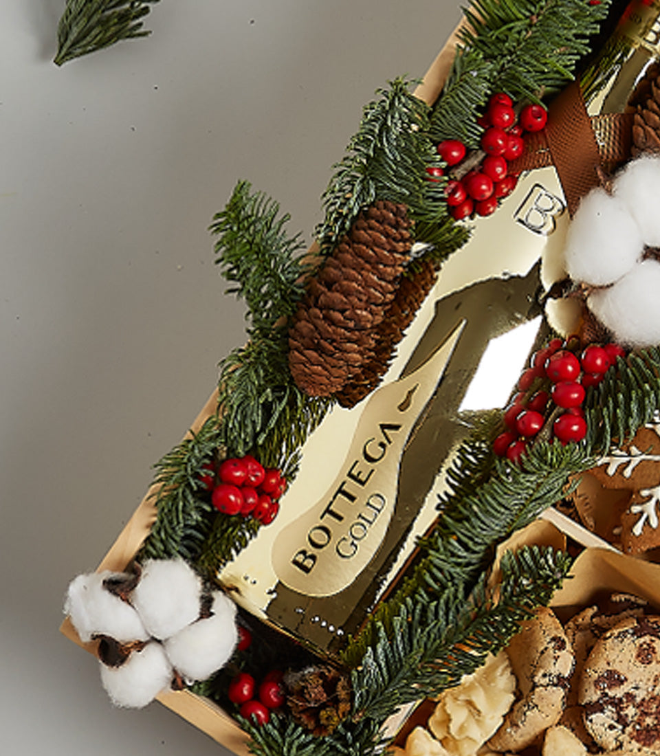 Gold sparkling wine gift box with gourmet cookies, pine branches, and festive berries for Christmas celebrations
