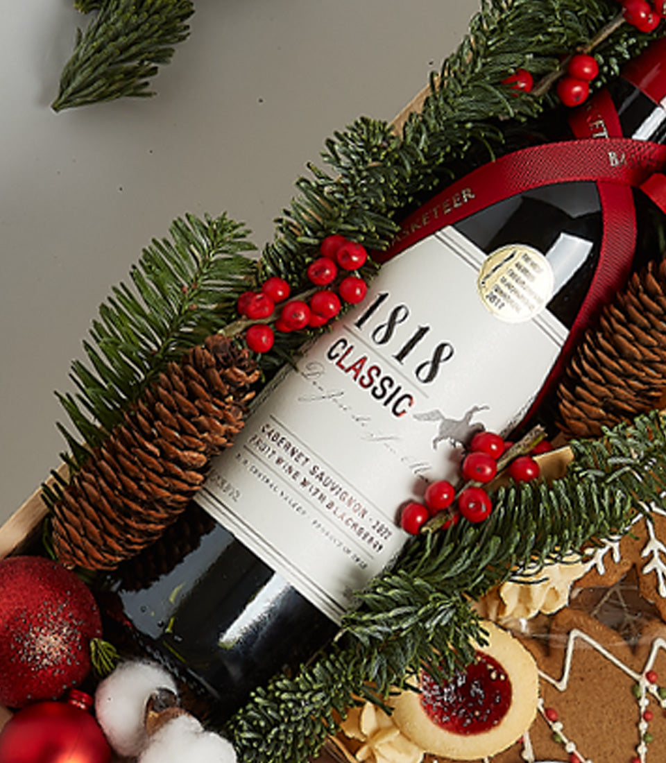Classic red wine and gingerbread cookie Christmas gift basket with festive pine and berries