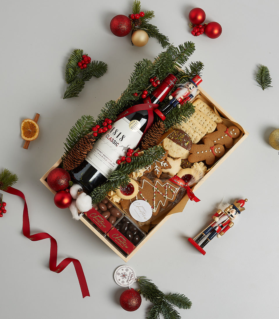 Premium red wine gift box with gingerbread cookies, chocolate, and festive pine decorations for Christmas