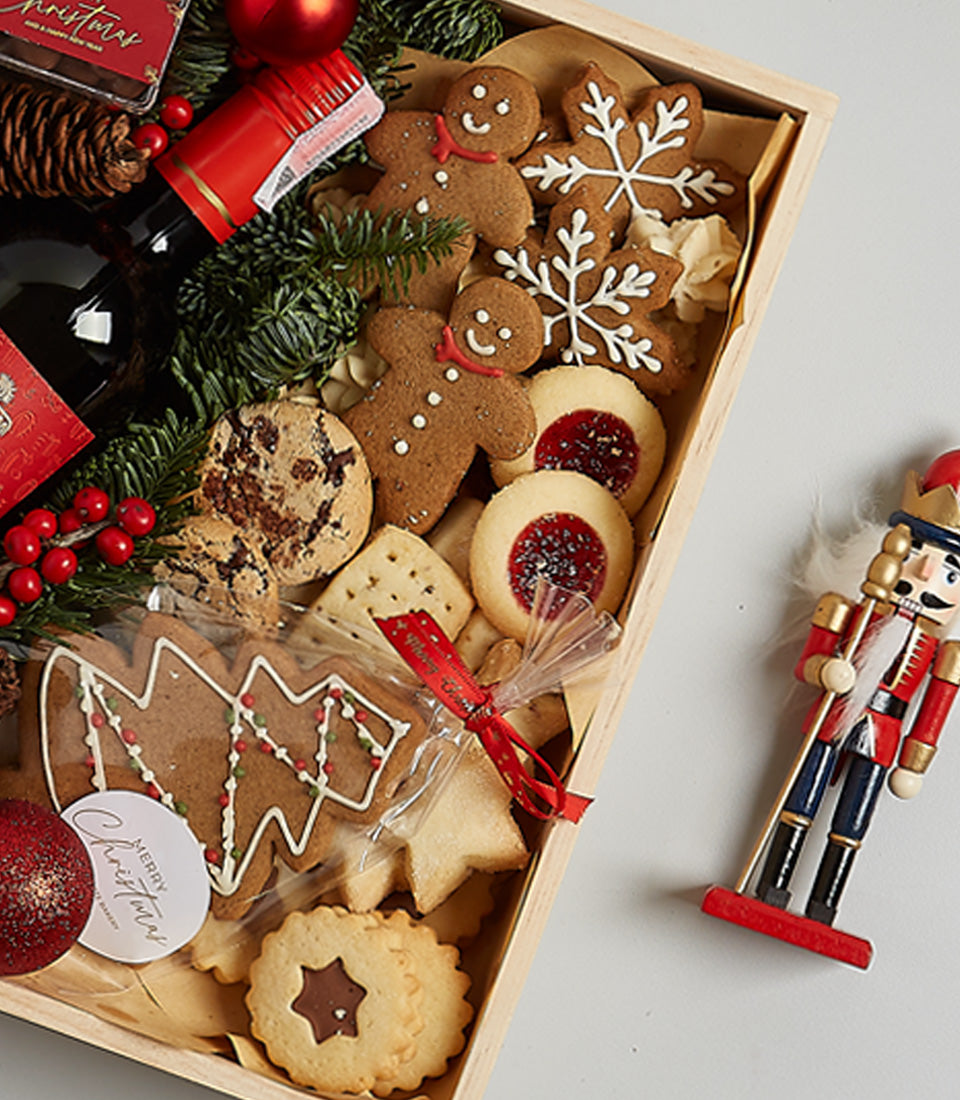 Festive wooden gift box with gingerbread cookies, shortbread, red wine, and Christmas ornaments