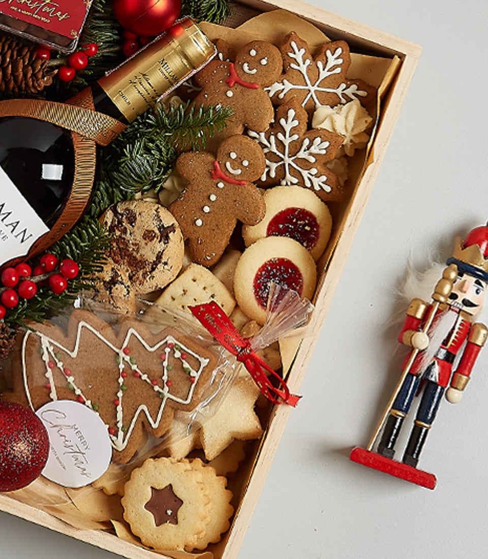 Festive wooden hamper with red wine, gingerbread cookies, snowflake biscuits, and Christmas decorations