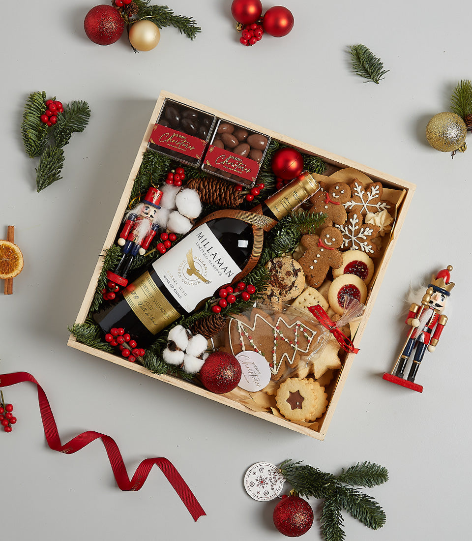 Festive red wine hamper with gourmet cookies, chocolates, and holiday decorations in wooden gift box