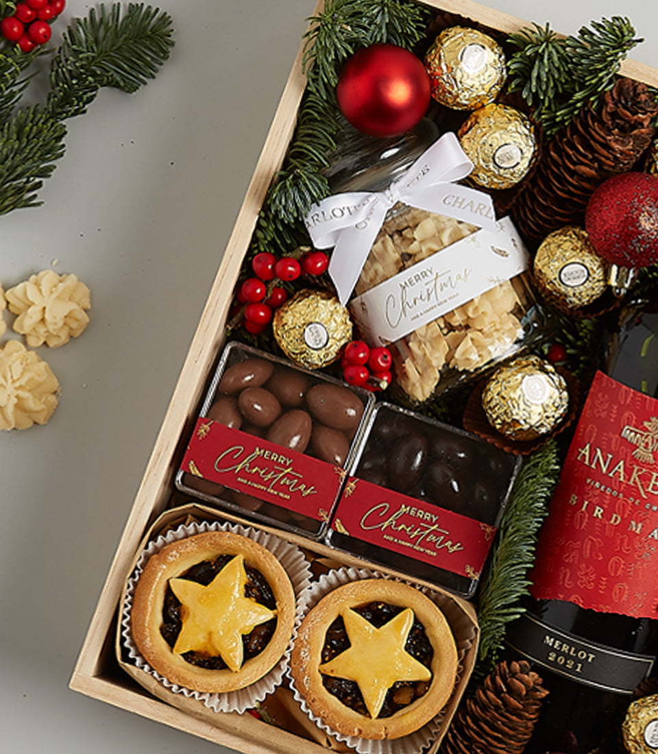 Festive Christmas wine hamper with red Merlot, mince pies, chocolates, and gold baubles in wooden gift box