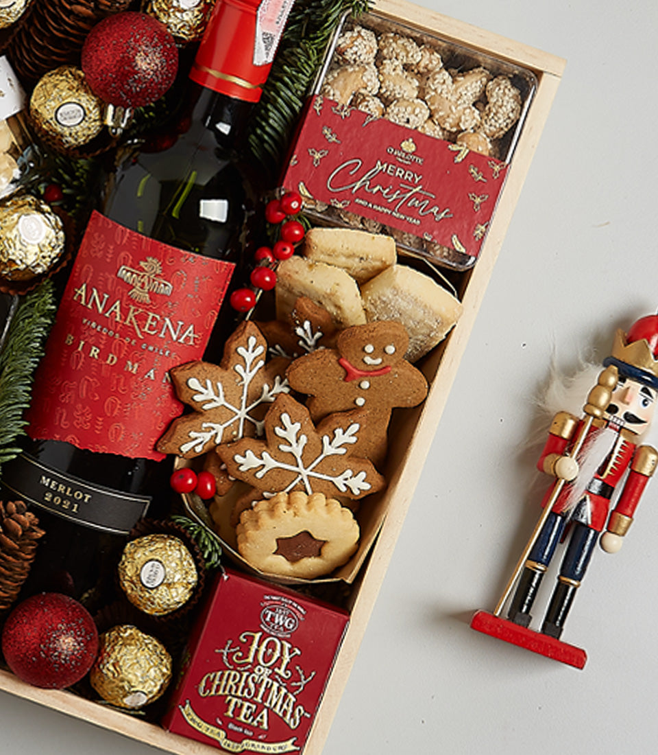 Festive Christmas hamper with red wine, gingerbread cookies, chocolates, and holiday tea in wooden crate