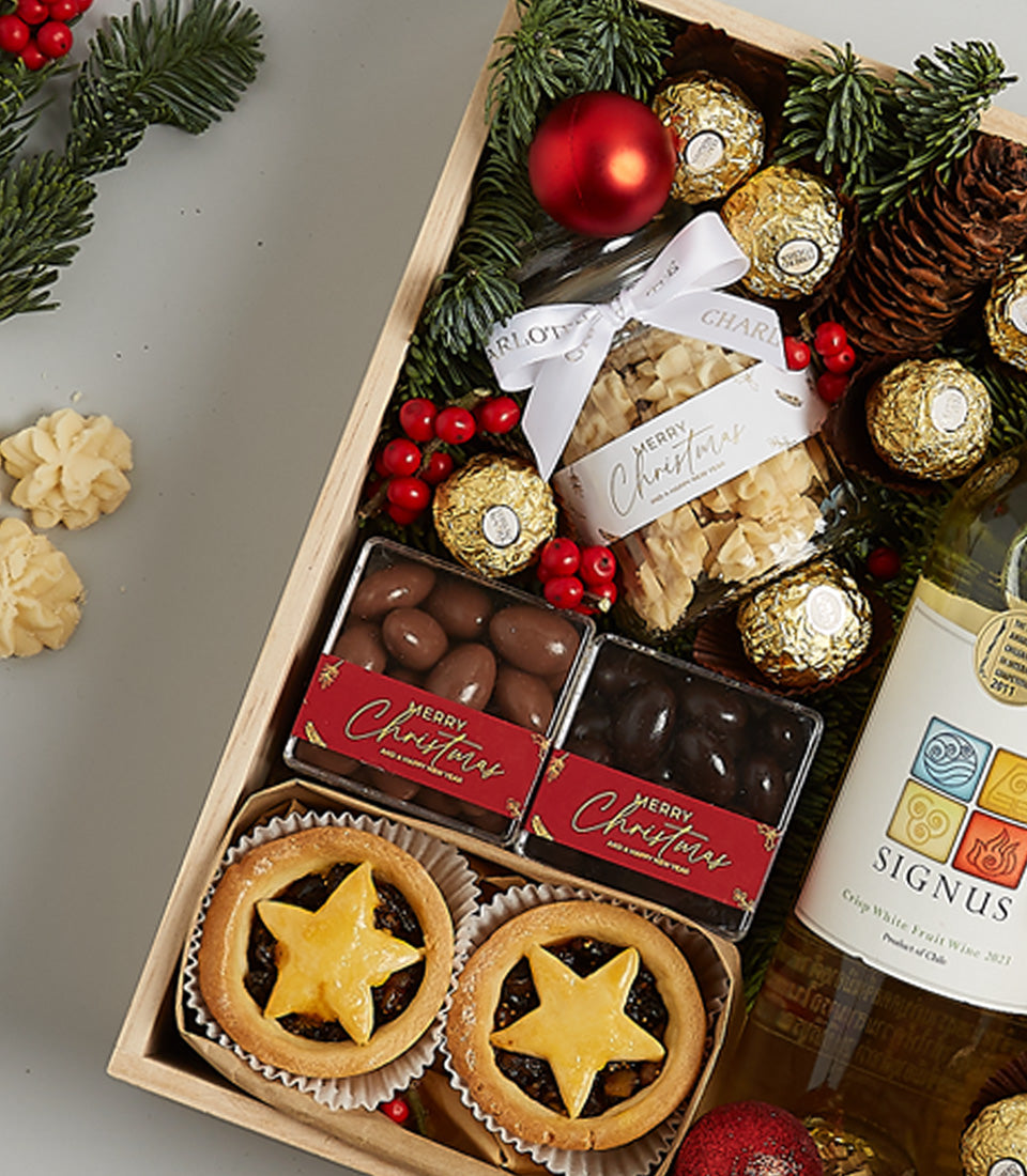 Festive wooden Christmas hamper with white wine, chocolates, mince pies, and almond brittle decorated with red baubles and