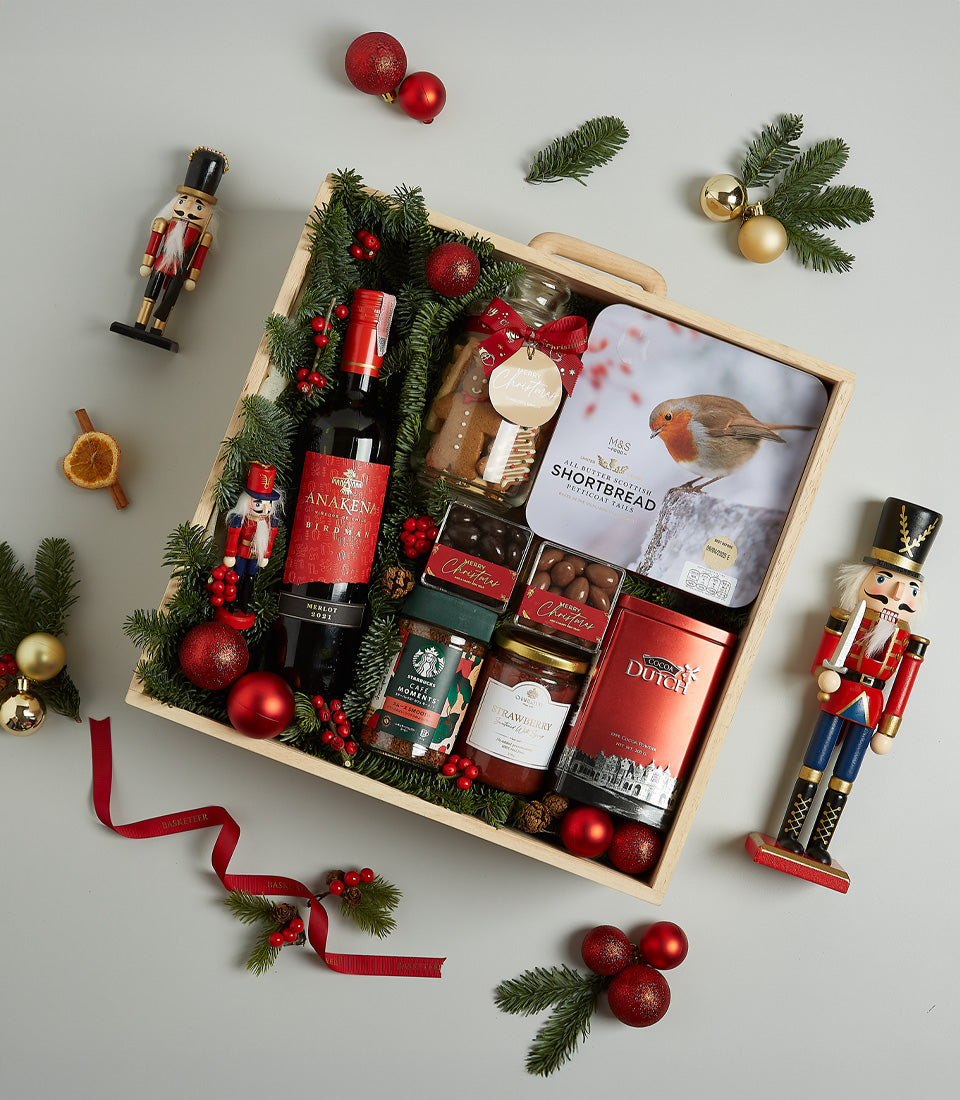 Luxury Christmas wine hamper with red wine, gourmet cookies, chocolates, and festive treats in wooden crate