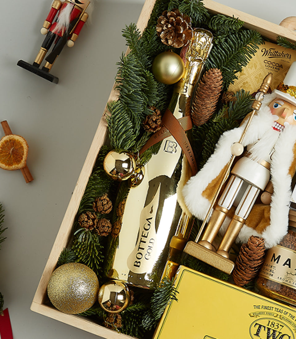 Luxury prosecco and treats Christmas hamper in wooden crate with chocolates, coffee, and festive gold decorations