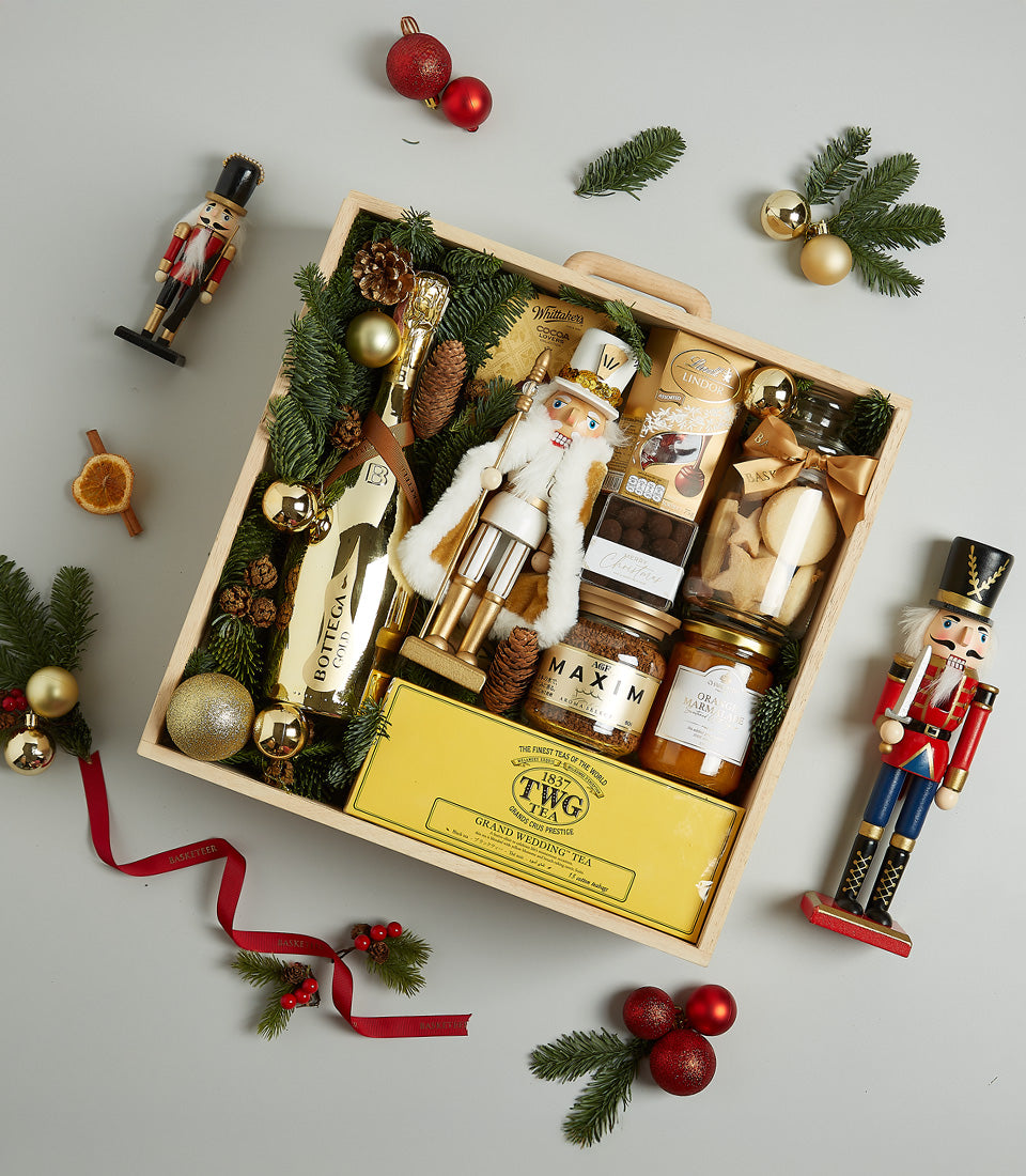 Luxury tea and gourmet treats Christmas hamper with prosecco, cookies, and chocolates in wooden crate with gold baubles and