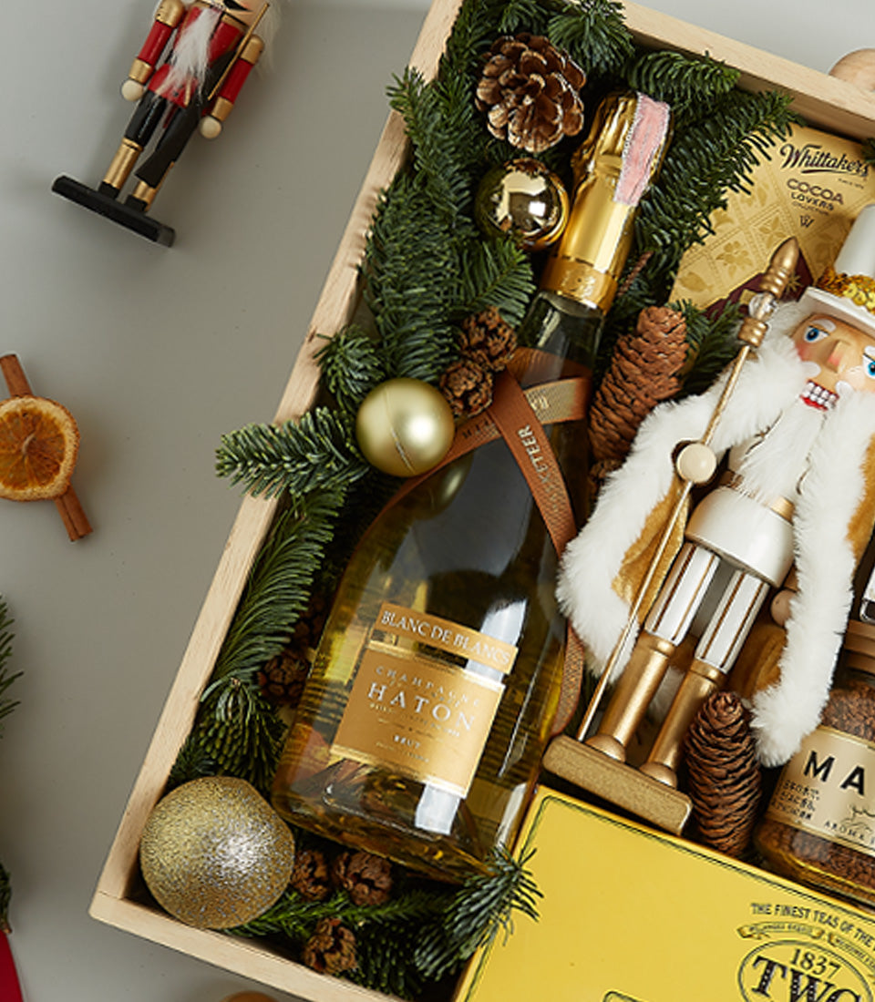 Festive golden luxury hamper with champagne, chocolates, and holiday decorations in wooden crate