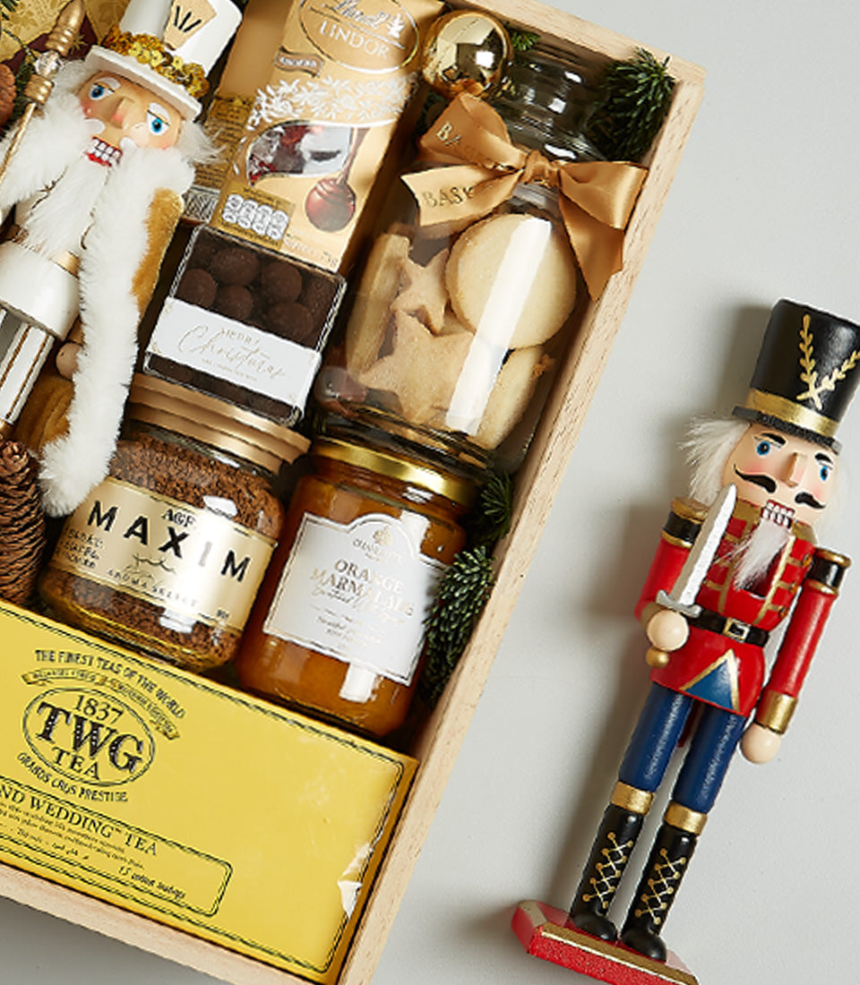 Festive Christmas hamper with prosecco, gourmet chocolates, coffee, and holiday nutcracker decoration in wooden crate