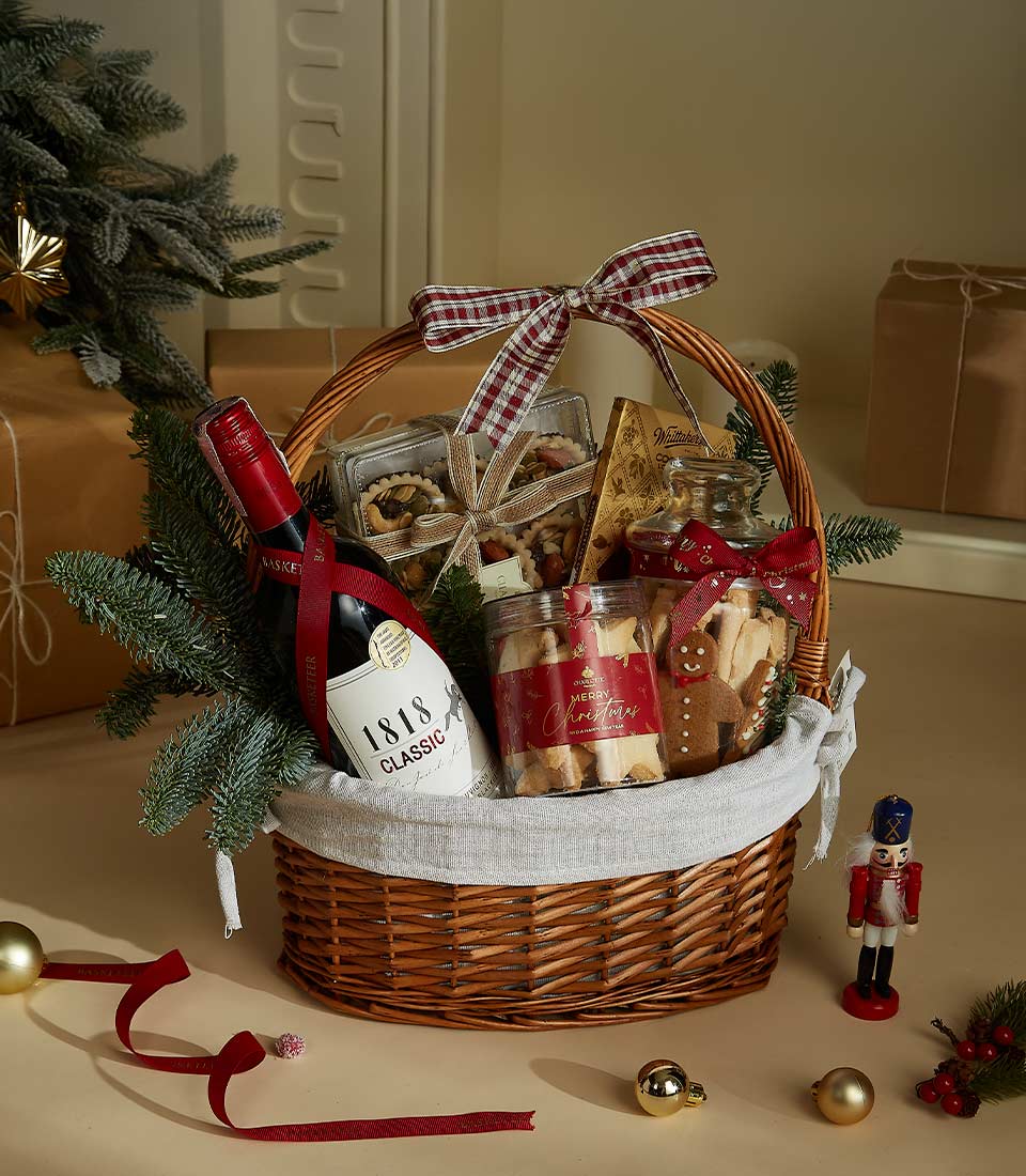 Festive holiday wicker basket with red wine, nuts, dried fruits, Christmas cookies, and plaid ribbon bow