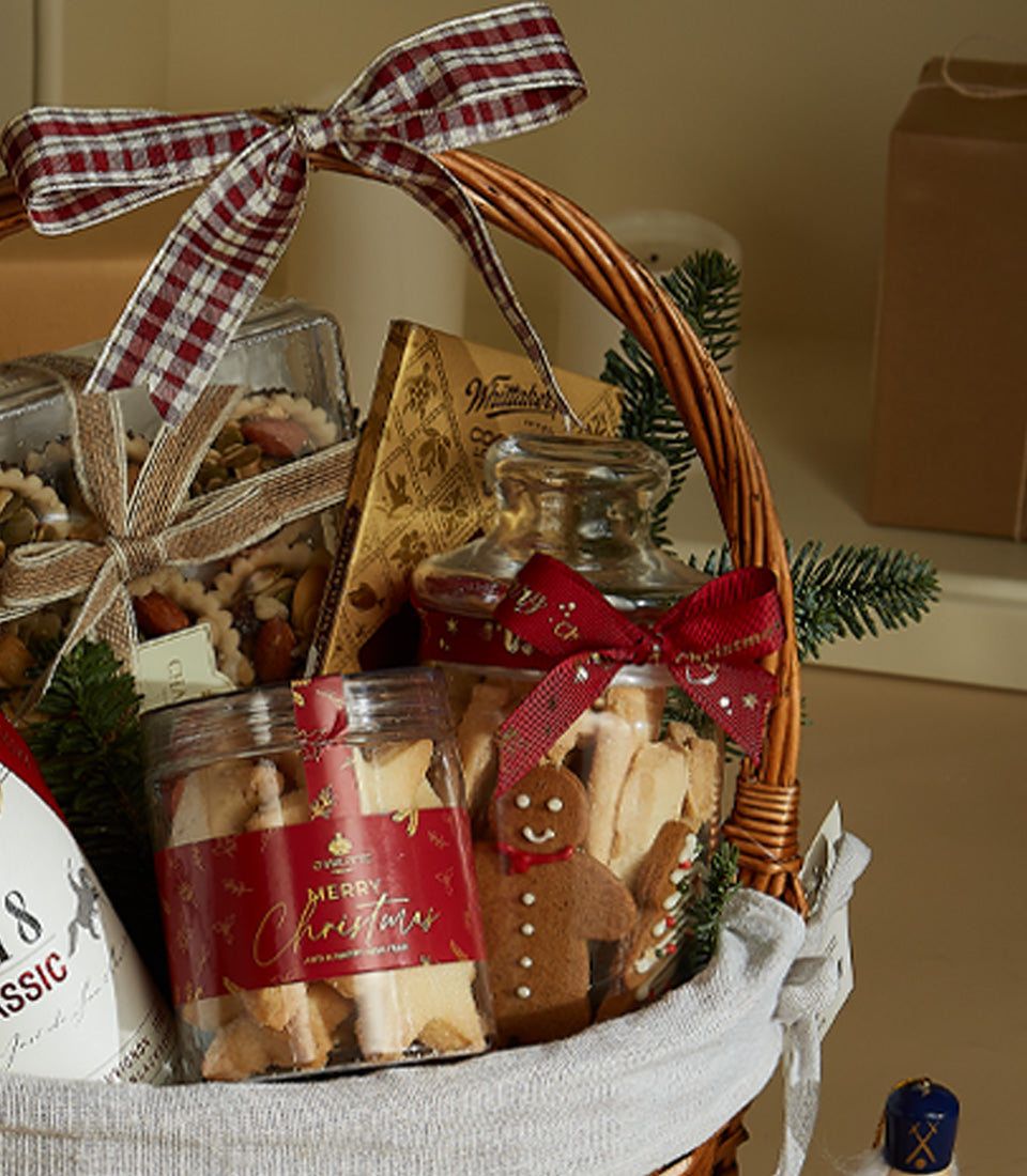Woven wicker festive basket with red plaid bow, filled with gourmet cookies, nuts, chocolates, and premium red wine for