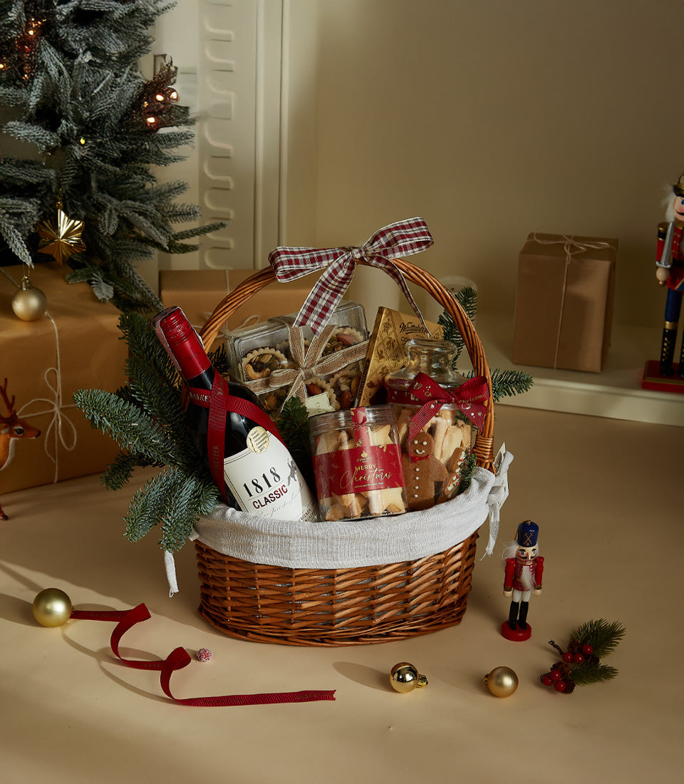 Woven wicker Christmas wine basket with red wine, gingerbread cookies, and festive plaid ribbon