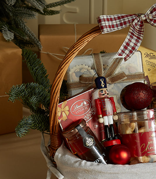 Basketeer holiday gift basket: Lindt chocolates, honey jar, and festive nutcracker in a wicker hamper with red plaid ribbon. Premium hamper delivery Thailand.
