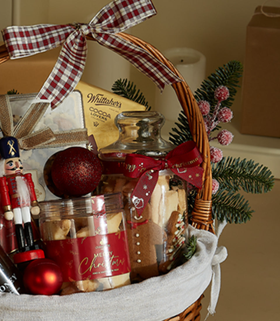 Basketeer holiday gift basket: wicker hamper with red plaid ribbon, Whittaker's chocolate, spiced cookies, and festive nutcracker. Premium hamper delivery Thailand.