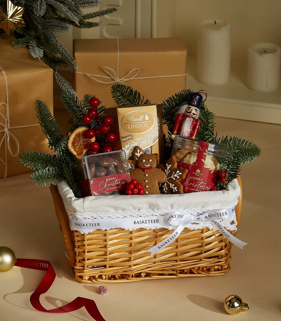 Woven wicker Christmas gift basket with Lindt chocolates, dark chocolate nuts, gingerbread cookies, and festive pine greenery