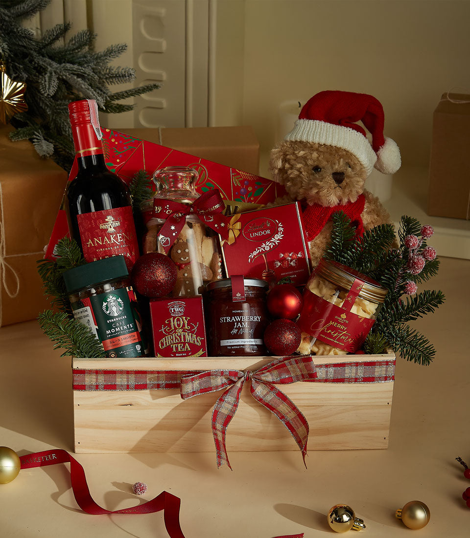 Festive wooden Christmas hamper with red wine, gourmet treats, and holiday decorations in plaid ribbon