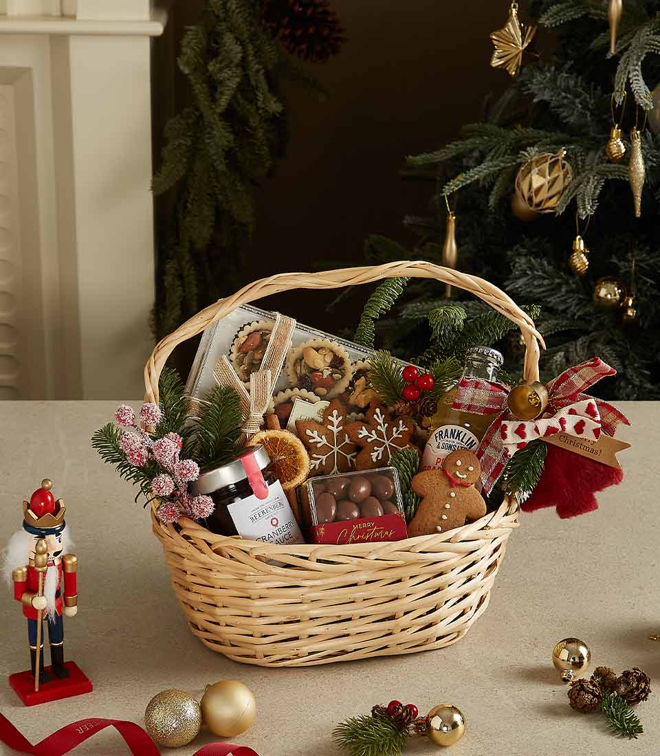 Woven wicker Christmas basket filled with gingerbread cookies, festive treats, cranberry sauce and holiday decorations with