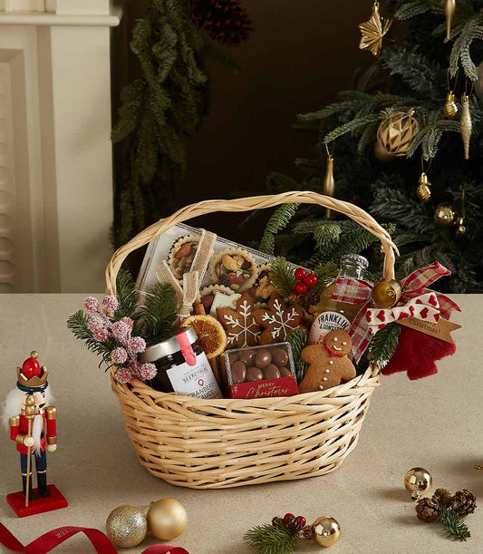 Woven wicker Christmas basket filled with gingerbread cookies, festive treats, cranberry sauce and holiday decorations with