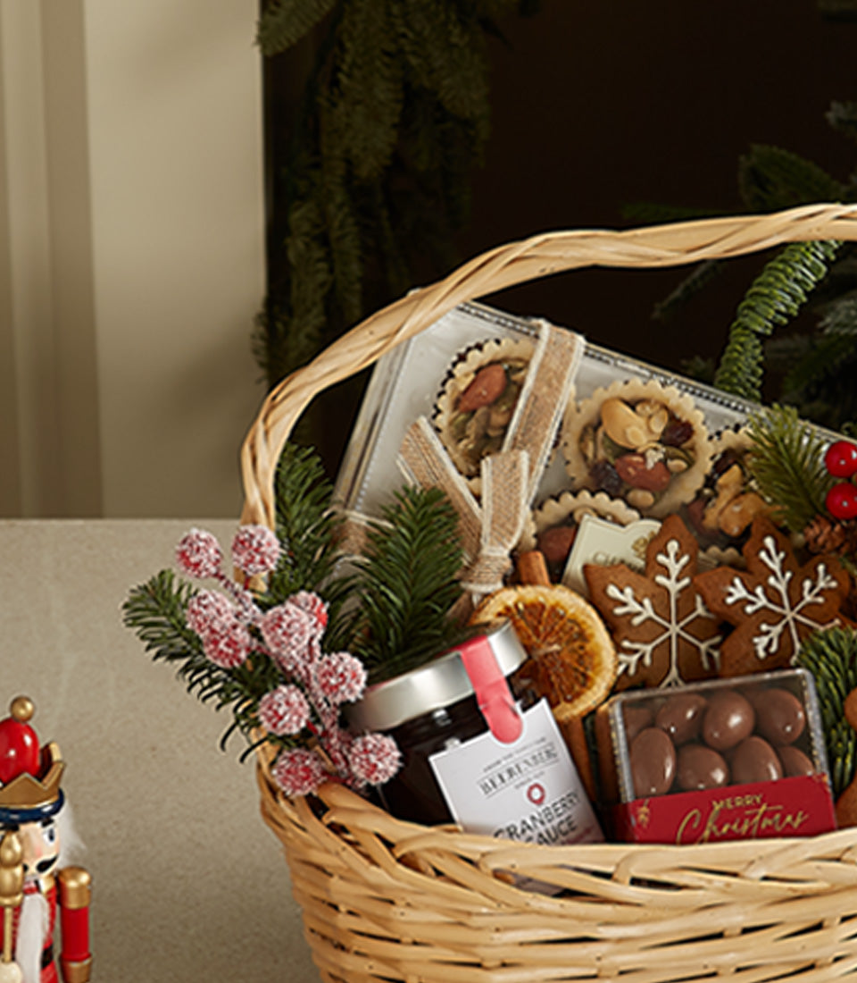 Woven wicker Christmas gift basket with gingerbread cookies, artisan tarts, cranberry sauce, chocolate treats, and festive