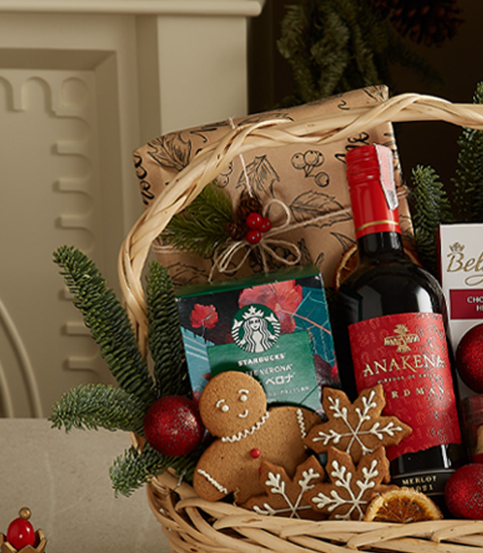 Festive luxury gift hamper with red wine, gourmet coffee, and gingerbread cookies in woven basket with holiday decorations