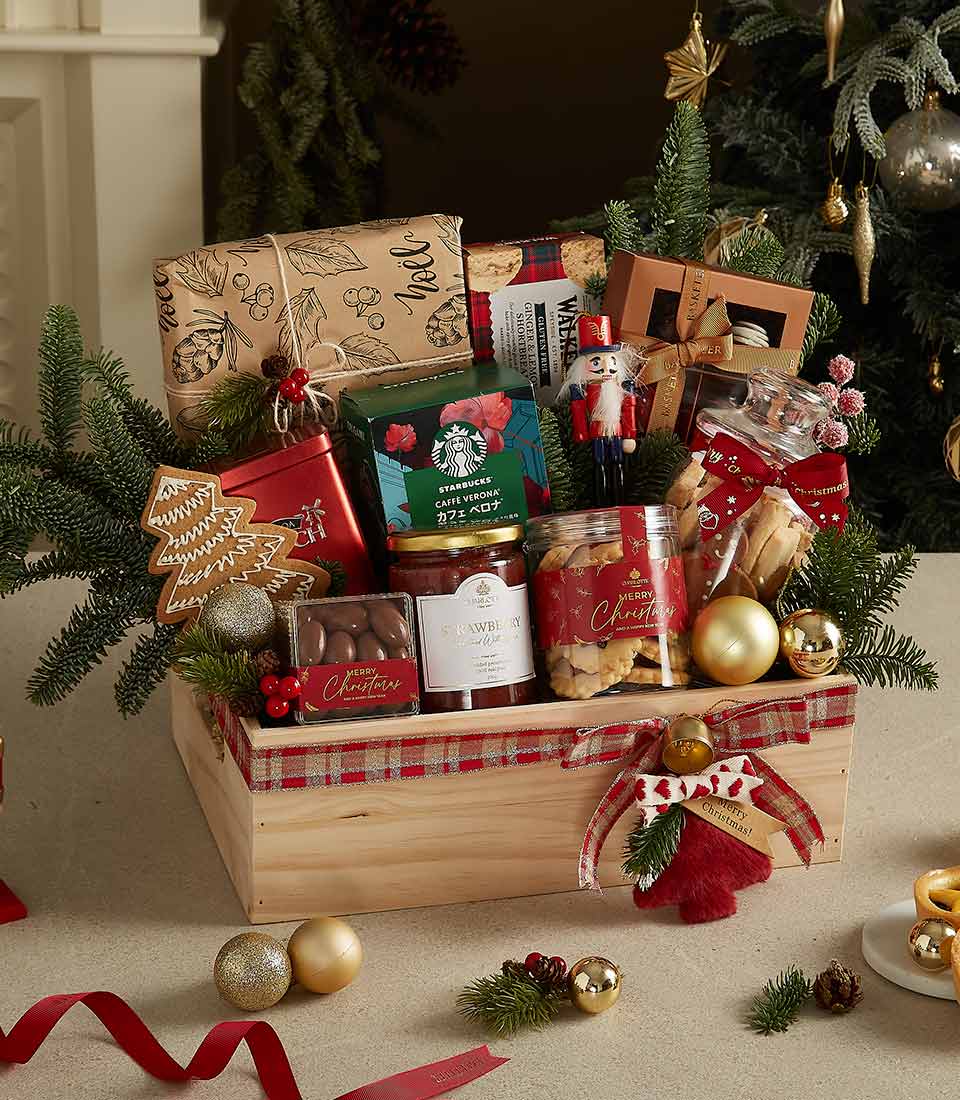 Festive gourmet gift crate with coffee, jam, cookies, shortbread, chocolates, pine branches, red berries, and gold baubles