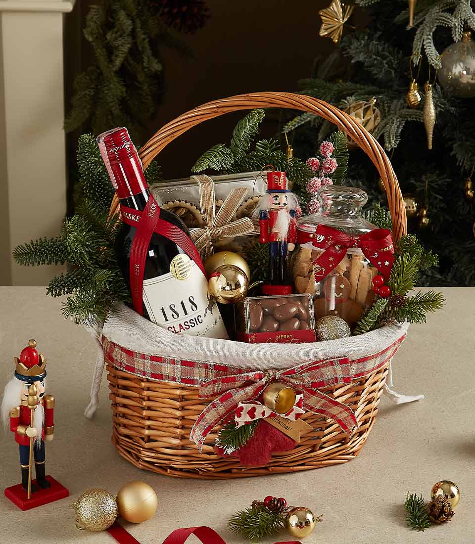Elegant wicker hamper with red wine, gourmet cookies, and holiday decorations tied with plaid ribbon