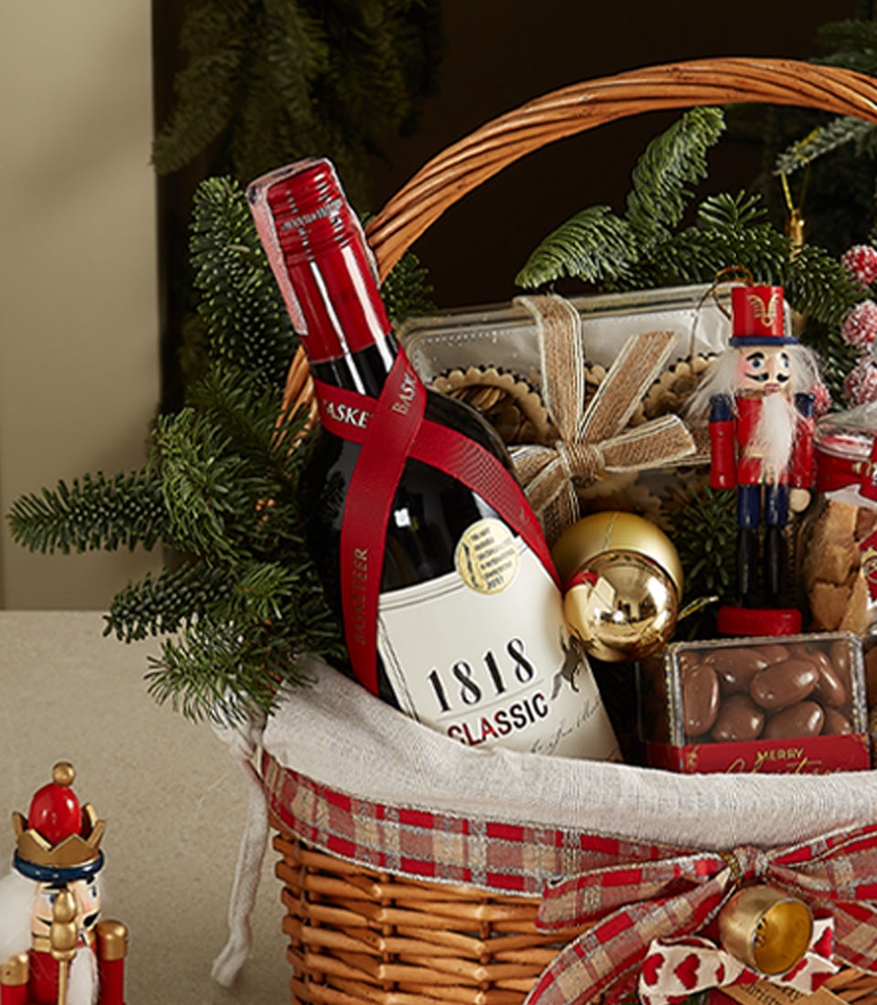 Elegant wicker Christmas hamper with red wine, festive cookies, chocolates, and holiday ornaments
