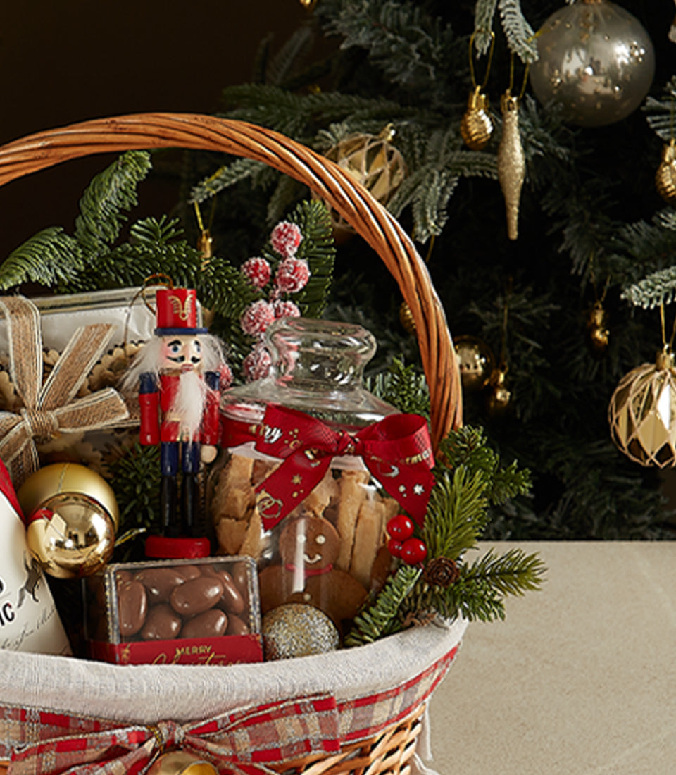 Woven wicker Christmas hamper with red plaid ribbon, gingerbread cookies, chocolate almonds, and festive nutcracker