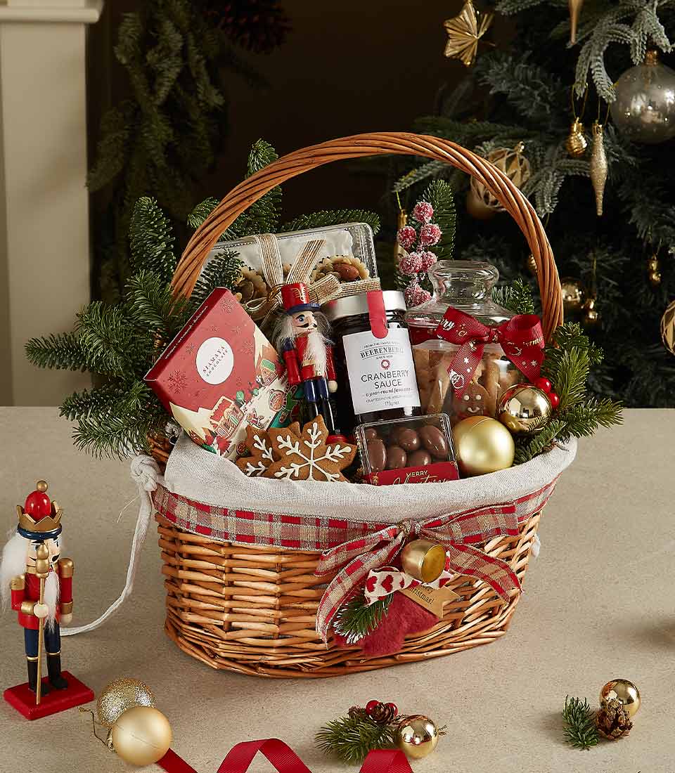 Woven wicker Christmas gift basket with red plaid ribbon, filled with gourmet chocolates, cranberry sauce, cookies, and