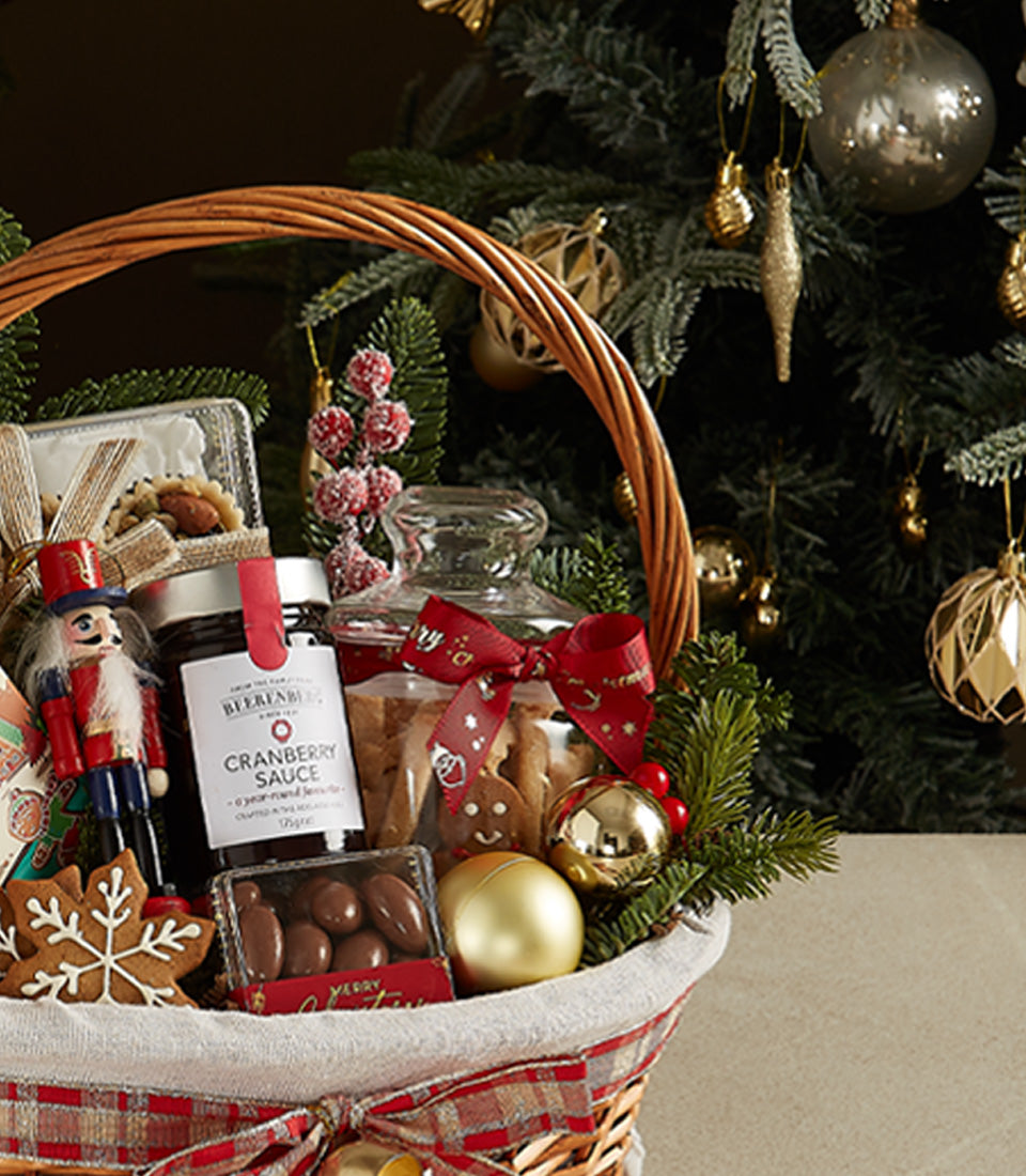 Festive wicker Christmas gift basket with cranberry sauce, cookies, chocolate treats, and holiday ornaments