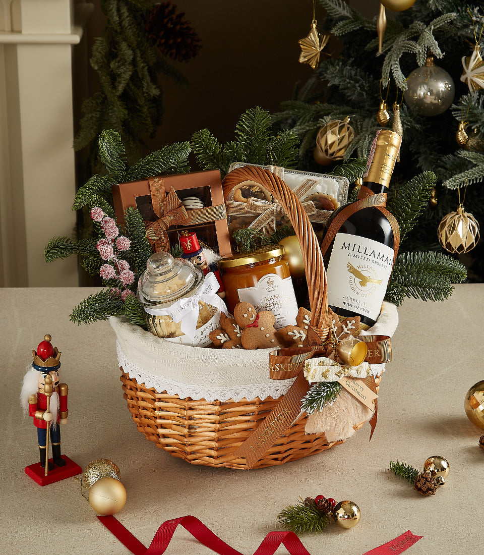 Festive wicker Christmas gift basket with red wine, orange marmalade, cookies, chocolates, and gingerbread treats