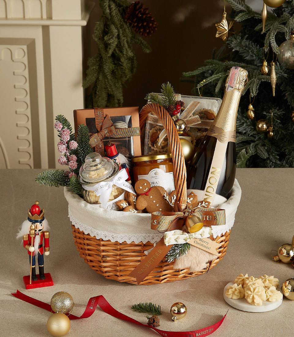 Festive Christmas gift basket with champagne, marmalade, cookies, and chocolates in wicker with gold ribbons and pine sprigs