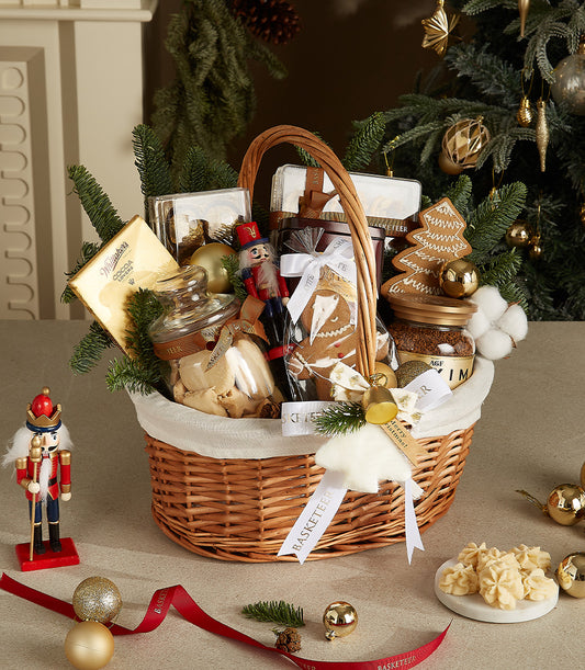 White wicker Christmas gift basket with gold chocolates, cookies, coffee, nutcracker, and gold baubles