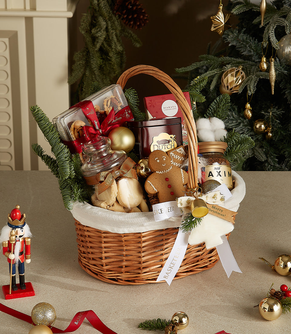 Woven Christmas gift basket filled with pastries, chocolate, coffee, and gingerbread, decorated with gold baubles and white