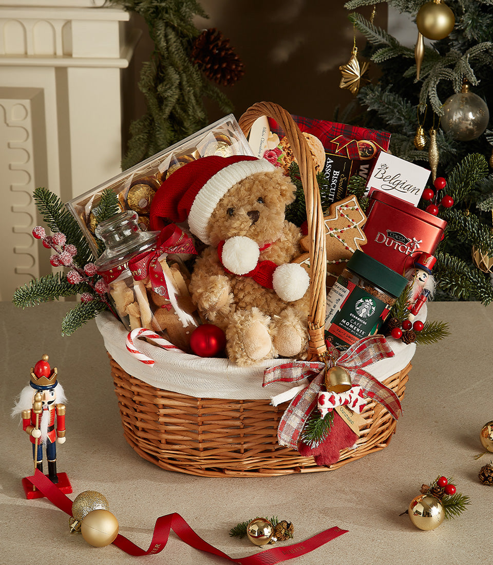 Festive Christmas gift basket with Santa teddy bear, chocolates, cocoa, coffee, and biscuits in wicker with red plaid ribbon