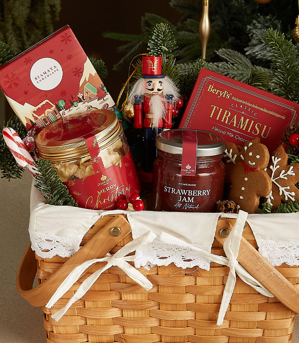 Woven wicker Christmas gift basket with festive treats, chocolates, cookies, jam, and holiday ornaments tied with white