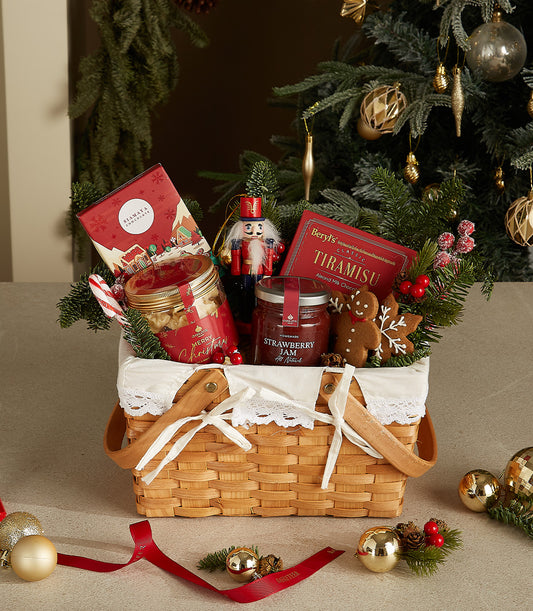 Woven Christmas gift basket with gourmet chocolates, jam, cookies, and festive decorations tied with white ribbon